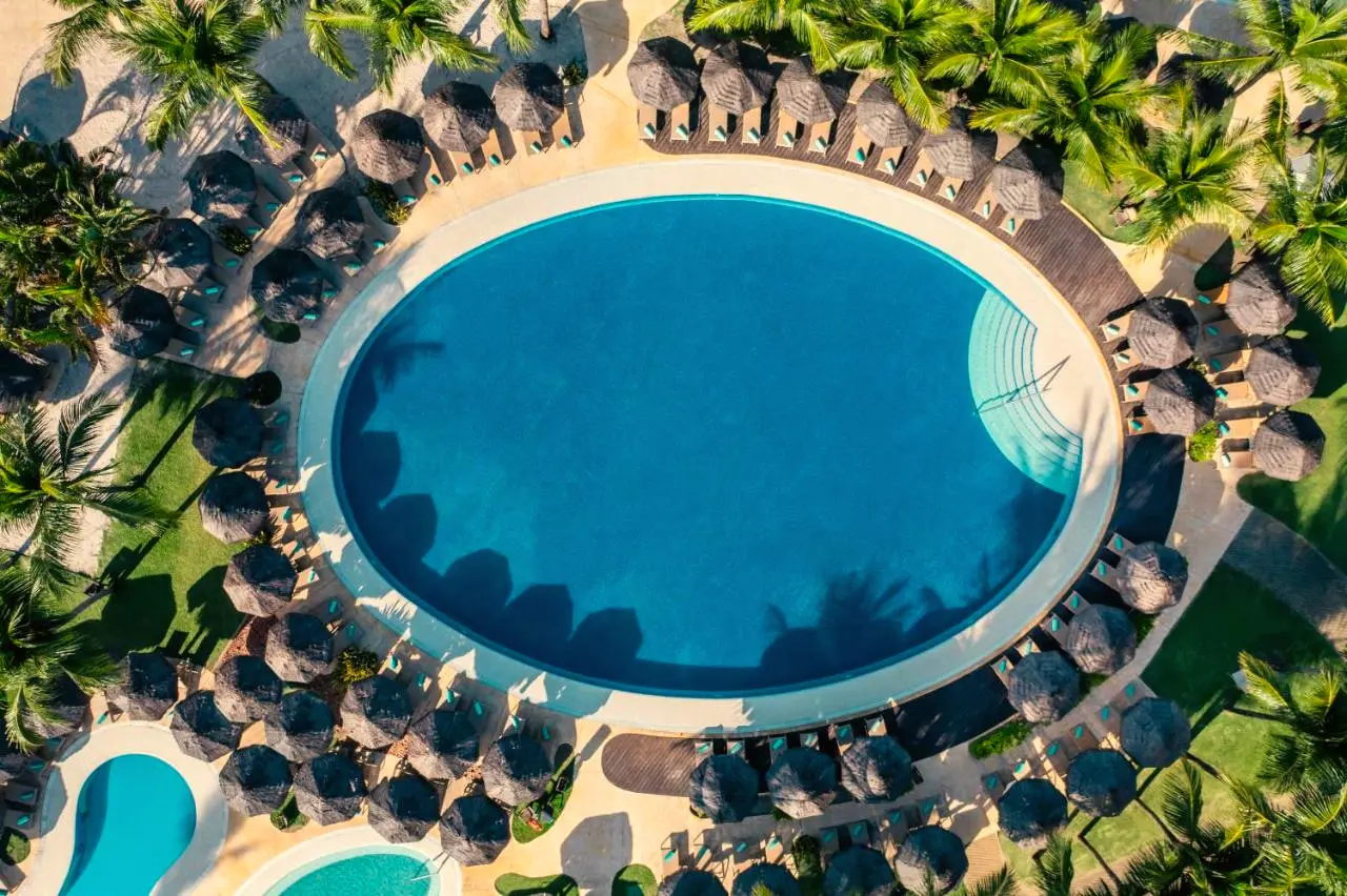 Vista aérea de piscina redonda cercada de guarda-sóis de palha