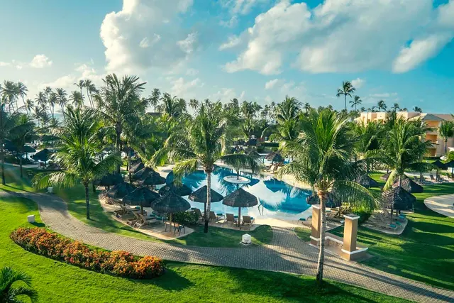 Jardins, caminhos e piscinas com guarda-sóis de palha entre coqueiros